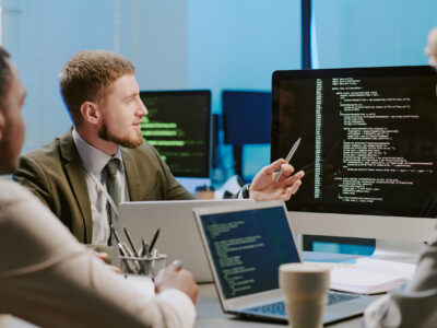 Group of three diverse young cybersecurity specialists discussing issues during meeting in office equipped with modern computers